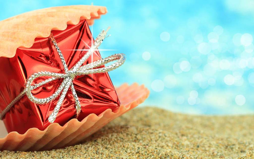 pacchetto regalo rosso inserito in una conchiglia sulla sabbia