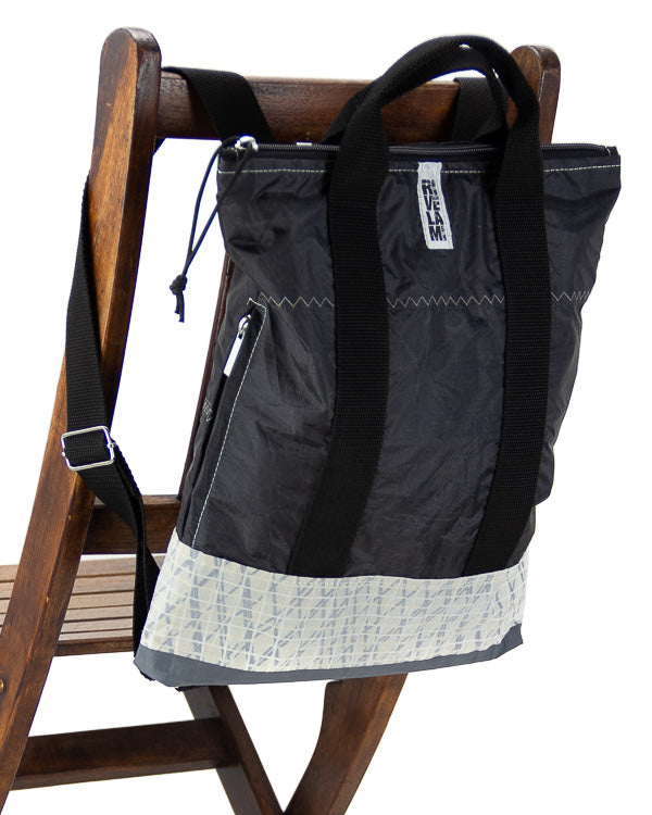 zaino piccolo nero in tessuto tecnico con tasca laterale appoggiato sullo schienale di una sedia in legno