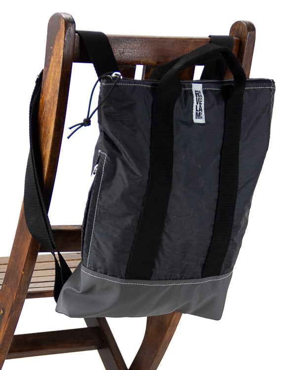 zaino piccolo in tessuto tecnico colore nero appoggiato su schienale di una sedia di legno